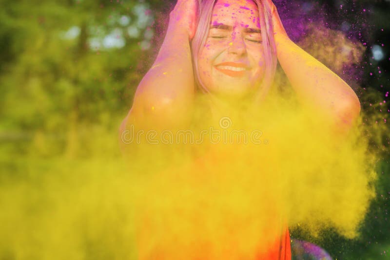 Closeup portrait of joyful blonde woman having fun in a cloud of yellow and purple dry Holi paint. Closeup portrait of joyful blonde model having fun in a cloud stock images